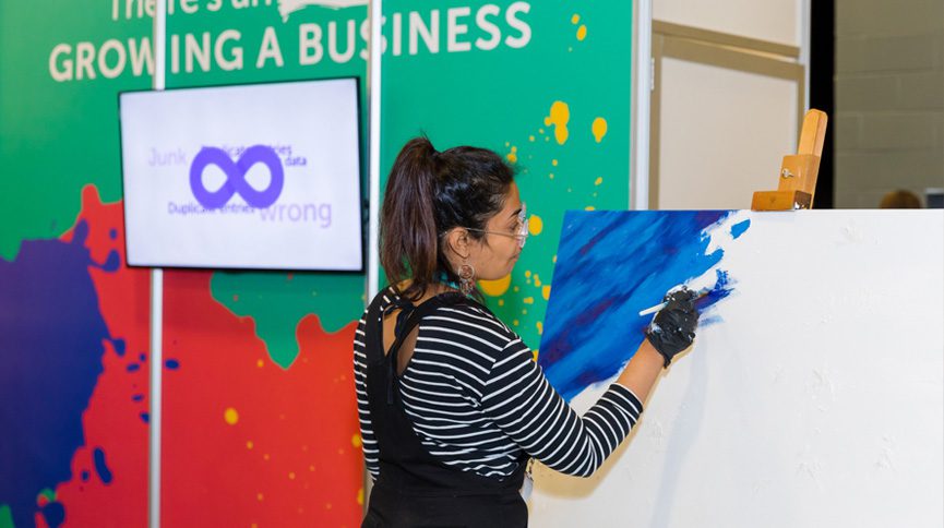 A woman painting on canvas at the eMerge Americas tech event.