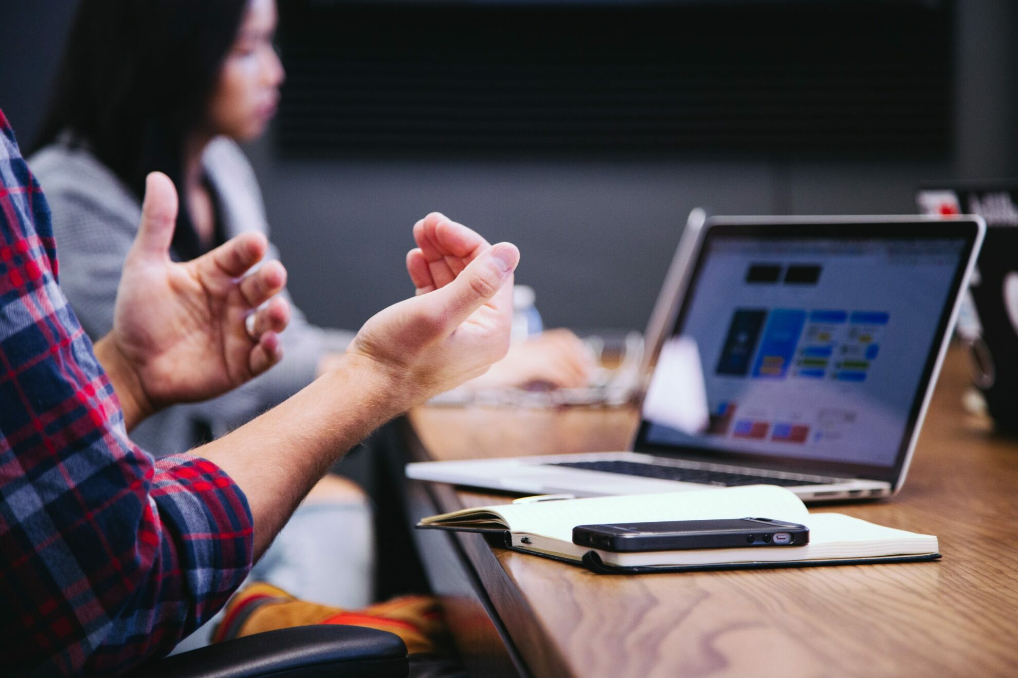 Person explaining relationship data for legal marketing at conference room table next to team member with a computer and smart phone in front of them