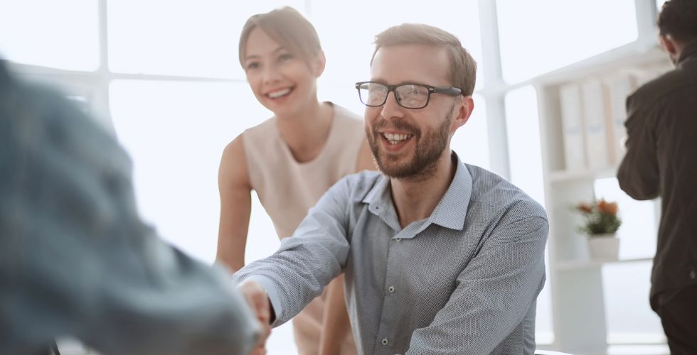 Business professionals smiling and shaking hands with a client, showcasing successful B2B customer relationship management