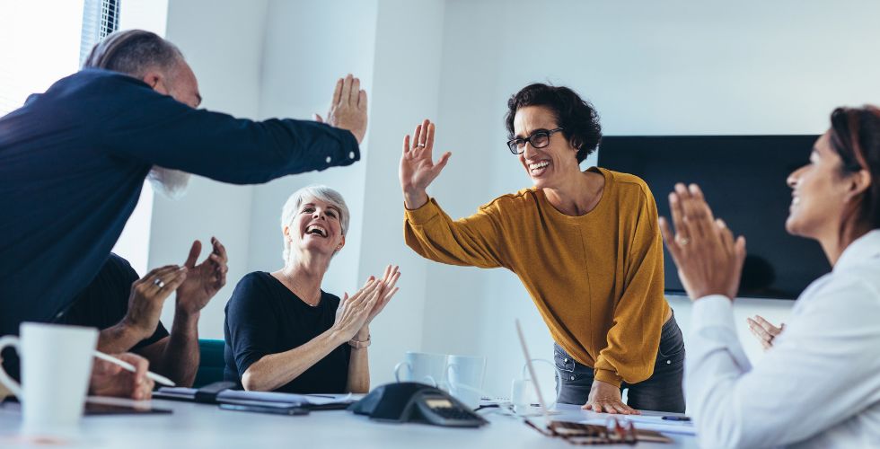 Team celebrating successful digital business transformation strategy with high-fives and applause in a modern office meeting.