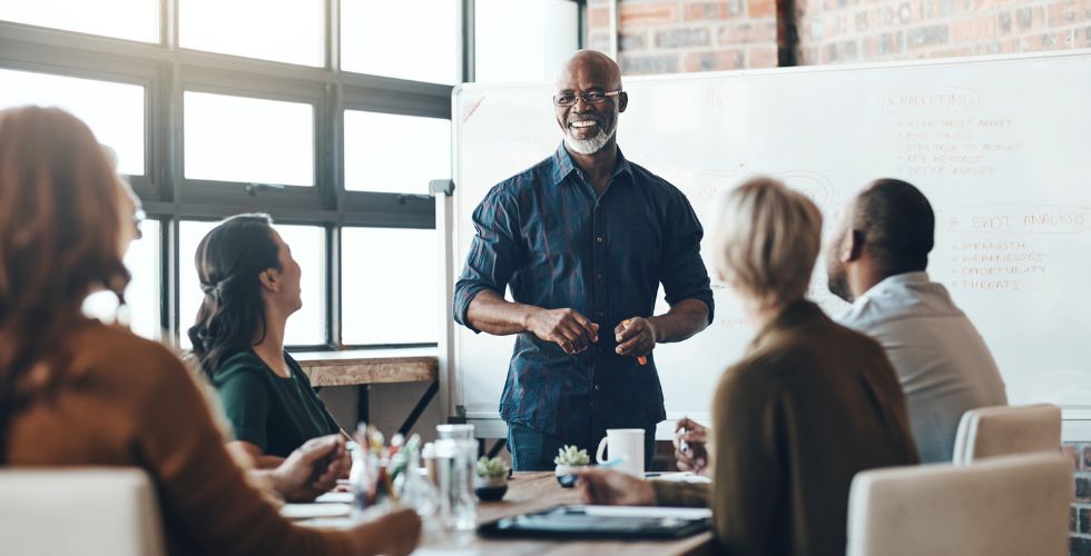 A business leader and colleagues discuss strategy in a team meeting, which highlights the difference between data and intelligence in using CRM for client insights and outreach.