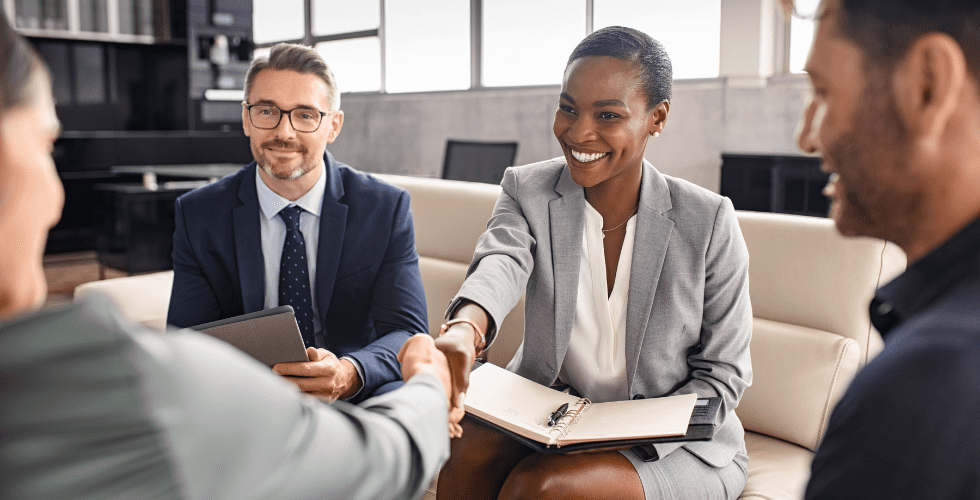 Two business professionals shaking hands across a table during a meeting, representing trust built on the difference between information technology, which focuses on keeping client data safe and organized, and artificial intelligence, which analyzes that data to make decisions that directly impact client relationships.