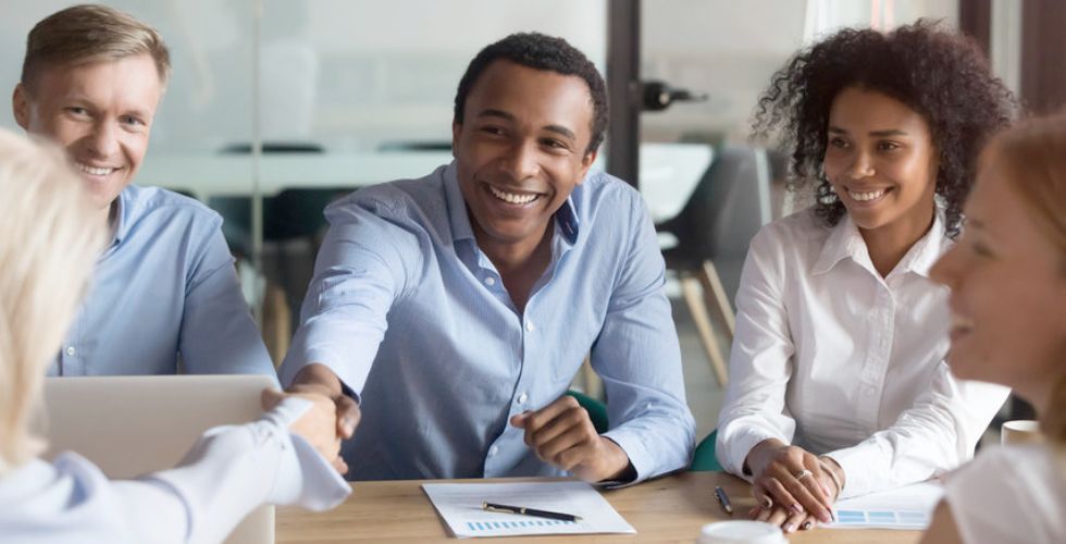 Diverse business professionals smiling and shaking hands during a meeting, symbolizing trust and connection — a key element in business relationship mapping.
