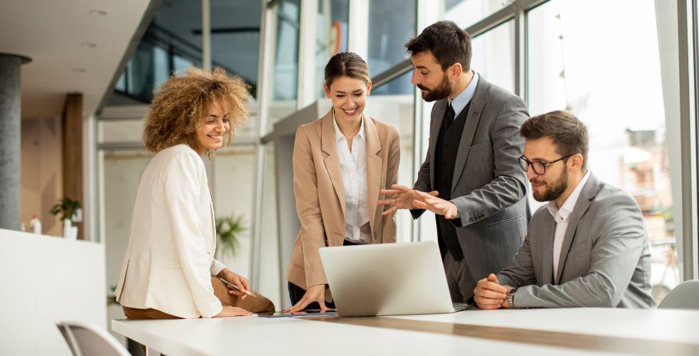 Team at a professional services firm collaborating around a laptop and discussing how data enrichment services like Introhive’s solutions enhance client insights and business development.