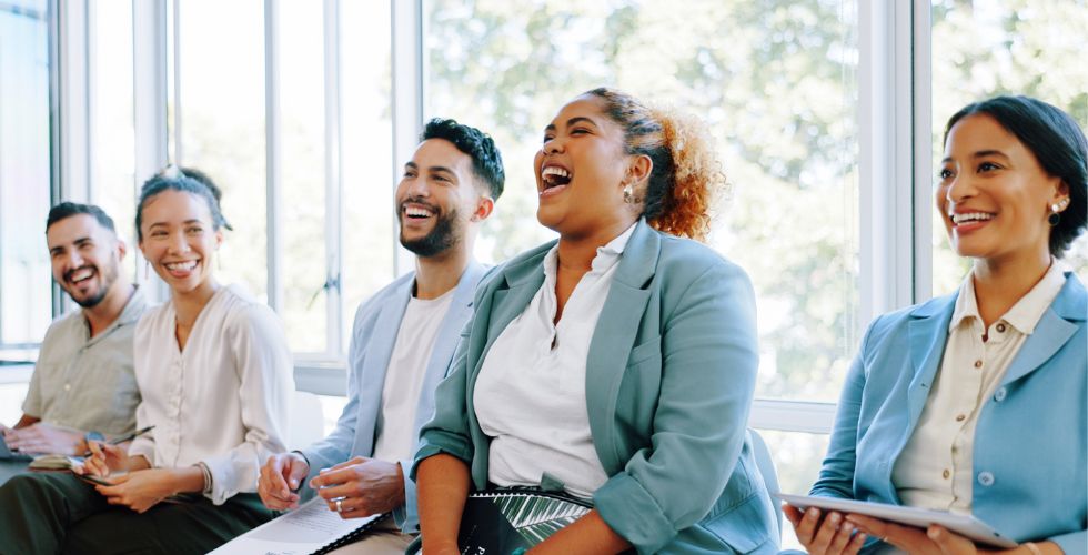 A diverse group of professionals sitting together in a bright office, smiling and engaged during a presentation about legal marketing tools and modern tech strategies.